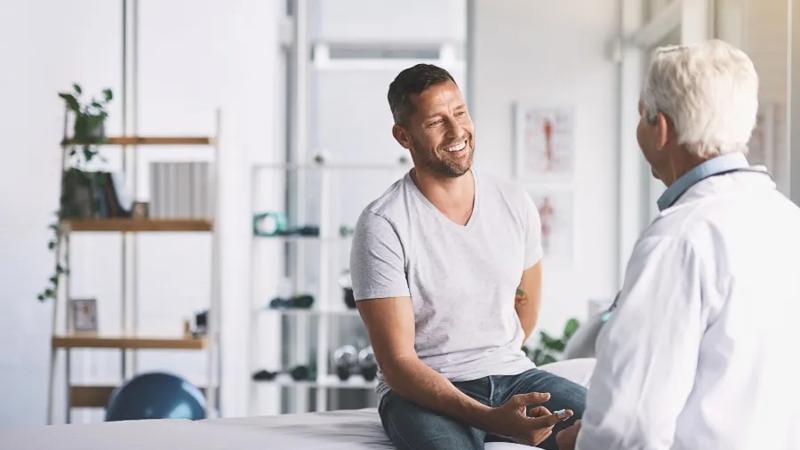 male patient speaking to doctor while sitting on examination table