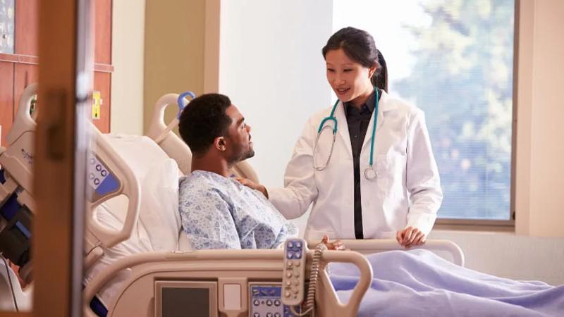 Female doctor talking with male patient in hospital bed