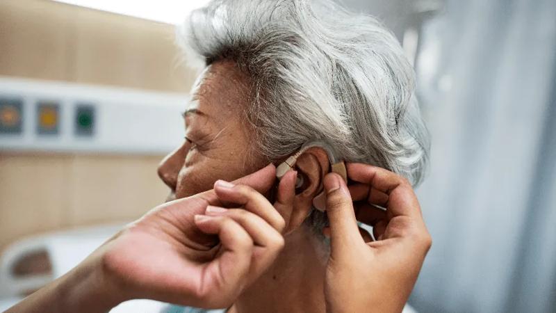 Physician placing hearing aid into the ear of an older woman.